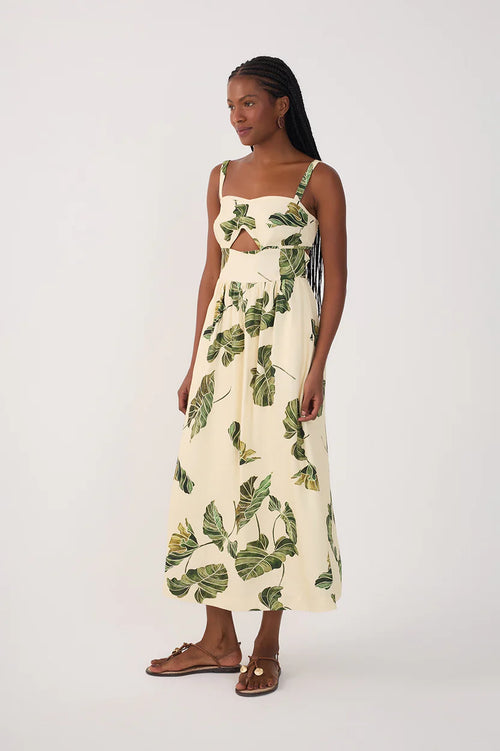 Woman wearing a cream-colored dress with green leaf patterns and a keyhoe at bust on a plain background