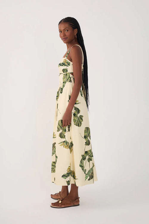 Side view of a woman wearing a cream-colored dress with green leaf patterns on a plain background