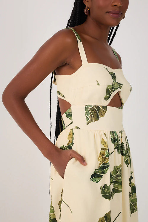 Woman wearing a cream-colored dress with green leaf patterns and a keyhole at bust on a plain background