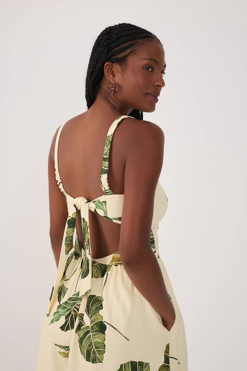 Woman wearing a cream-colored dress with green leaf patterns on a plain background