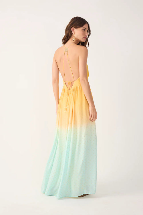 Woman wearing a yellow to light blue gradient maxi dress with an open back on a white background