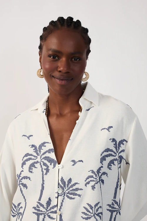 Woman wearing a collared white shirt with blue palm tree pattern on a plain background