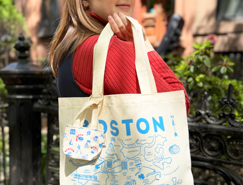Person holding a tote bag with 'Boston' map and icon designs outdoors