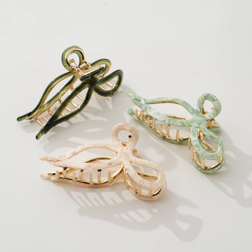 Three bow shaped hair clips in green, beige, and olive green on a light background