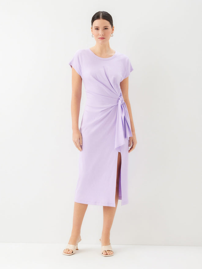 Front view of a woman wearing a light purple wrap dress and kitten heels with a plain background
