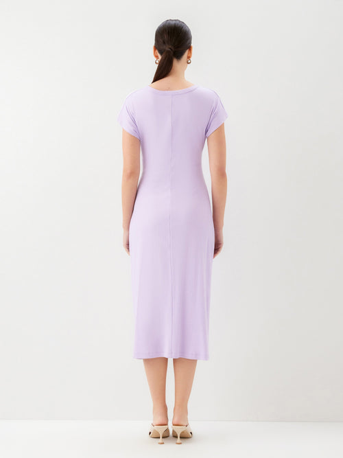 Back view of a woman wearing a light purple wrap dress and kitten heels with a plain background