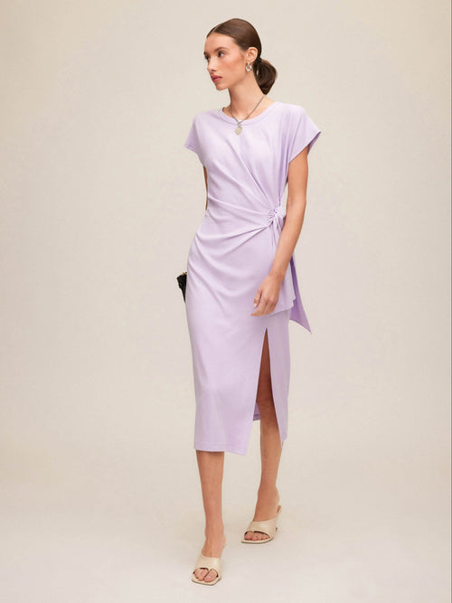 Woman wearing a light purple wrap dress and kitten heels with a plain background