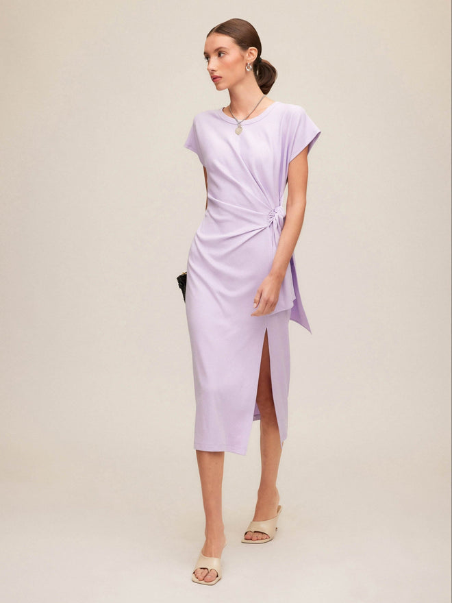 Woman wearing a light purple wrap dress and kitten heels with a plain background