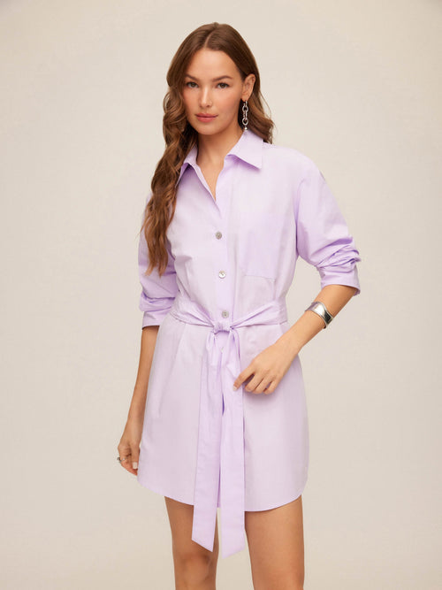 Woman wearing a short light purple dress with a belt on a beige background