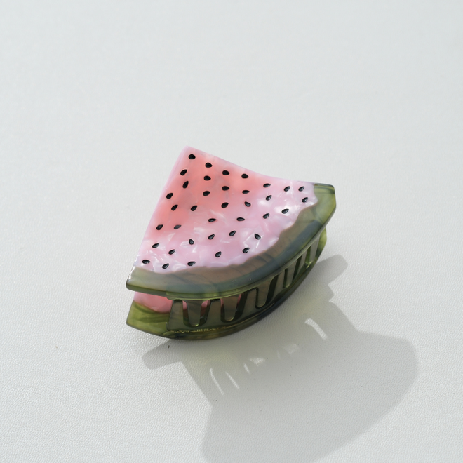 Watermelon hair clip with pink flesh and black seeds and green rim on a white background