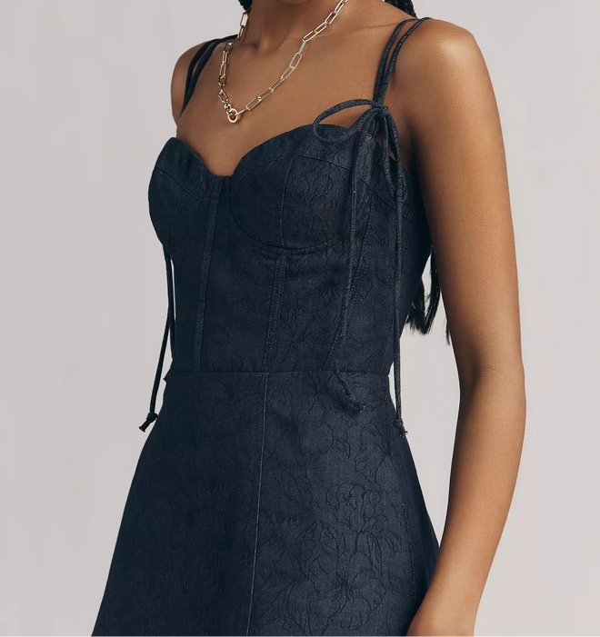 Woman wearing a dark blue dress with thin straps against a plain background