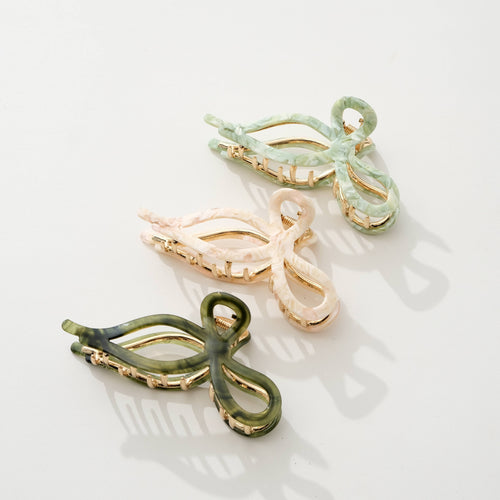 Three bow shaped hair clips in green, beige, and olive green on a light background
