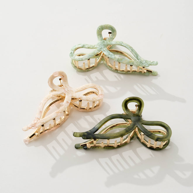 Three bow shaped hair clips in green, beige, and olive green on a light background
