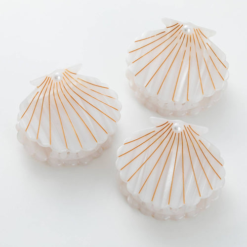 Three shell-shaped hair clips with gold lines on a white background