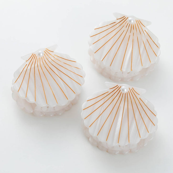 Three shell-shaped hair clips with gold lines on a white background