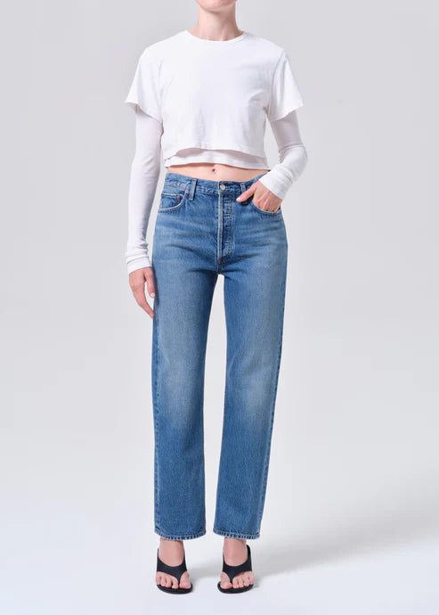 Person wearing a white cropped top and medium wash blue jeans on a light gray background