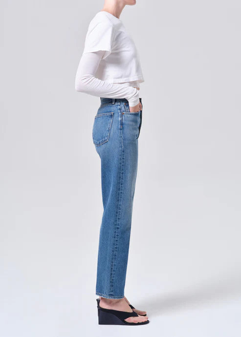 Side view of a woman wearing medium wash blue jeans, black wedge heels and a white top on a plain background