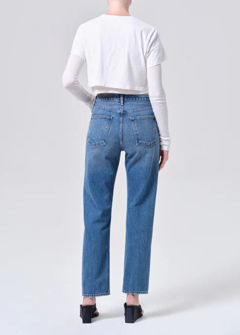 Back view of a woman wearing medium wash blue jeans and layered white tops with black wedge heels