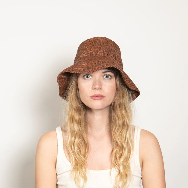 Woman wearing a brown straw bucket hat against a plain background