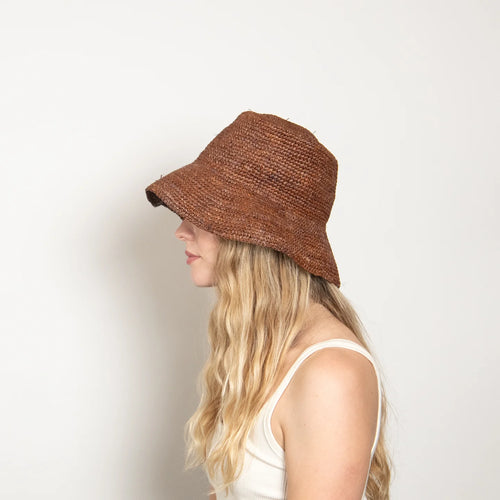 Side view of a woman wearing a brown straw bucket hat against a plain background