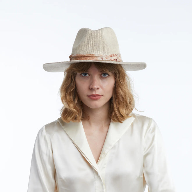 Woman wearing a cream straw hat and white blouse against a white background