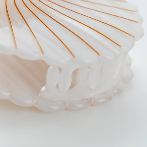 Close up of a shell-shaped hair clip with gold lines on a white background