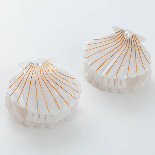 Two shell-shaped hair clips with gold lines on a white background