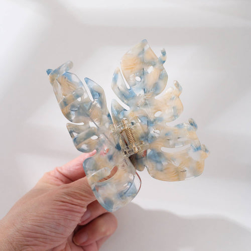 Butterfly-shaped hair clip with a marble pattern held by a hand on a white background