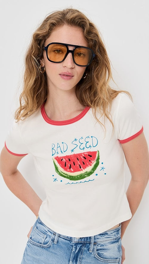 Woman wearing a white t-shirt with a watermelon graphic and 'Bad Seed' text, paired with blue jeans, gold earrings and sunglasses.